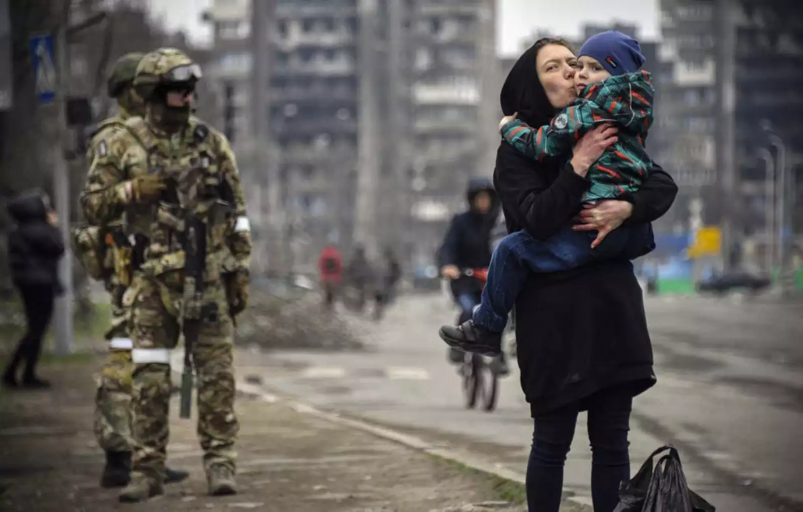 Una mujer sostiene y besa a un niño junto a soldados rusos en una calle de Mariupol el 12 de abril de 2022, mientras las tropas rusas intensifican una campaña para tomar la ciudad portuaria estratégica.