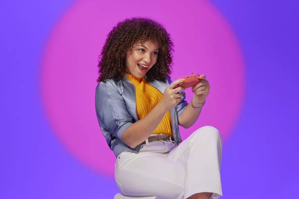 Mujer gamer sentada sosteniendo un control en la mano con una expresión divertida.