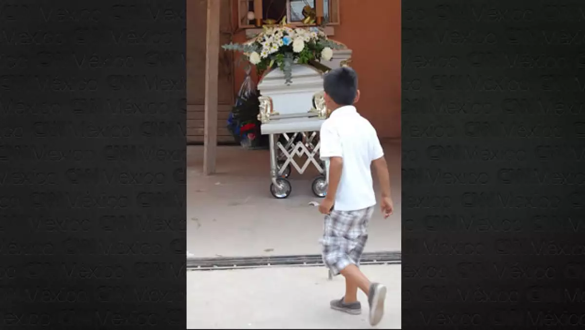 Un niño camina frente a un ataud