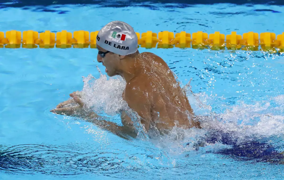 Foto de Miguel de Lara en la alberca de 200 m pecho con una gorra de natación que lleva la bandera de México y su apellido.