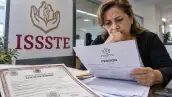 Mujer revisa documentos de pensión y un acta de matrimonio en una oficina, con el logotipo del ISSSTE visible en primer plano.