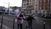 Dos manifestantes disfrazados corren mientras, al fondo, se observan nubes de gas lacrimógeno durante las protestas organizadas contra el aumento del costo de vida y la desigualdad, en París.