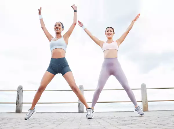 Jumping jack, fitness and women training cardio, happy with workout and smile during exercise in the city by the ocean.