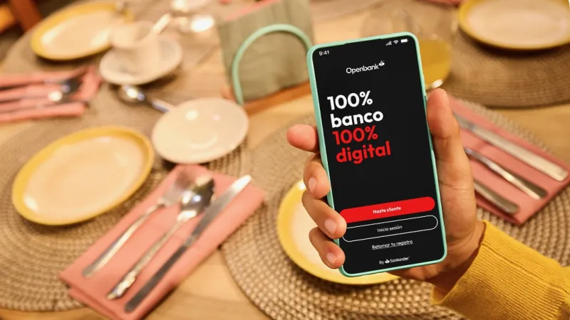 pantalla de un smartphone que muestra la app de Openbank, mientras una mano sostiene el teléfono por encima de una mesa con los cubiertos bien ordenados en un restaurante