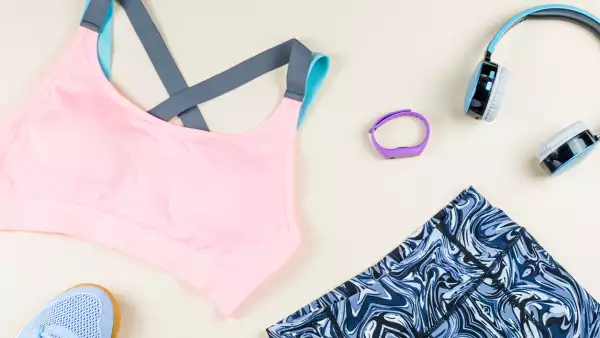 Woman sport bra, leggins, sneakers, headphones and fitness tracker on neutral background. Sport fashion concept.