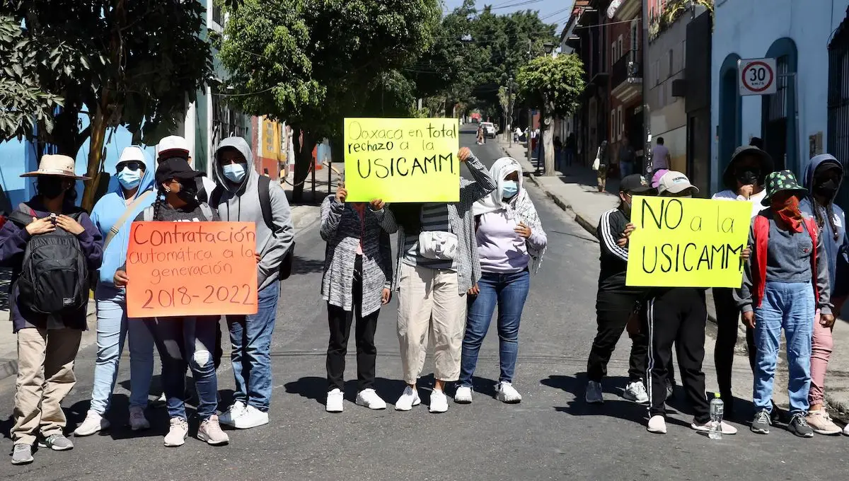 Normalistas Oaxaca protestan para exigir contratación inmediata y eliminación de la Usicamm. Sostiene cartulinas amarillas con sus mensajes de protesta.