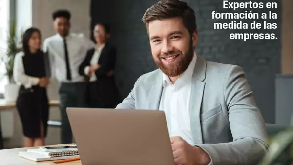 Hombre sonriendo y checando su laptop. Detrás se observan otras personas que lo están mirando.