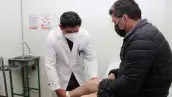 Un médico que viste bata blanca revisa la pierna de un paciente. 