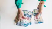 Vista cenital de las manos de una mujer contando billetes de 500 pesos mexicanos sobre un fondo blanco.