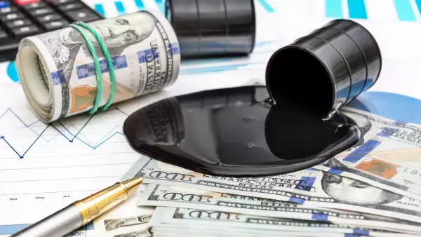 Spilled crude oil with money and calculator on financial graphs.