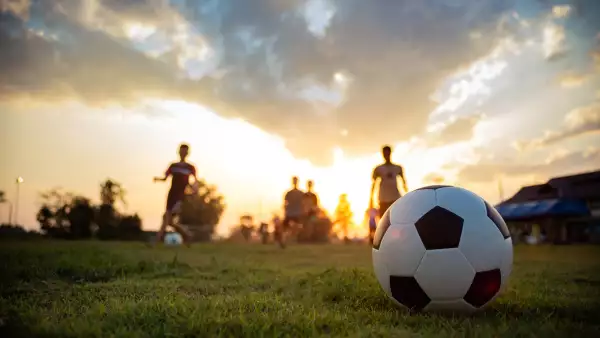 An action sport picture of a group of kids playing soccer football for exercise in community rural area under the sunset.