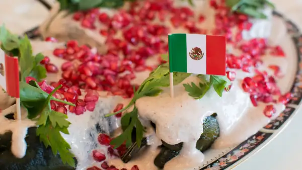 Tres chiles en nogada con dos pequeñas banderas insertadas con palillos sobre en un plato.jpg