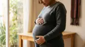 Mujer embarazada, se muestra sobre todo su panza de alrededor de 8 meses de gestación y ella la toca con ambas manos. 