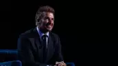 foto de david beckham sentado y sonriente con las manos entrelazadas al frente