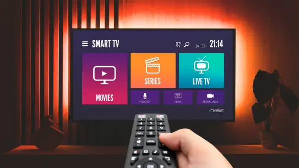 Una televisión mostrando el menú de streaming mientras un usuario con control en mano busca qué mirar.