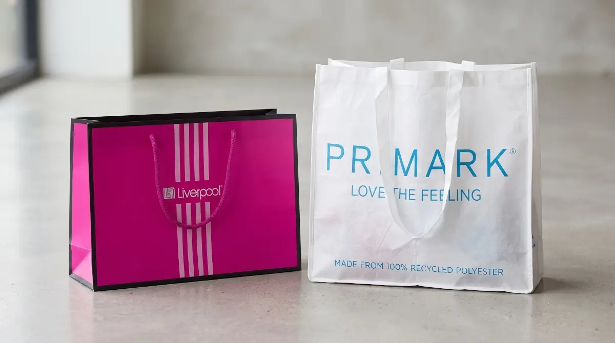 Dos bolsas de compras juntas: del lado izquierdo, una bolsa rosa de Liverpool y del lado derecho está una bolsa de tela de Primark. 