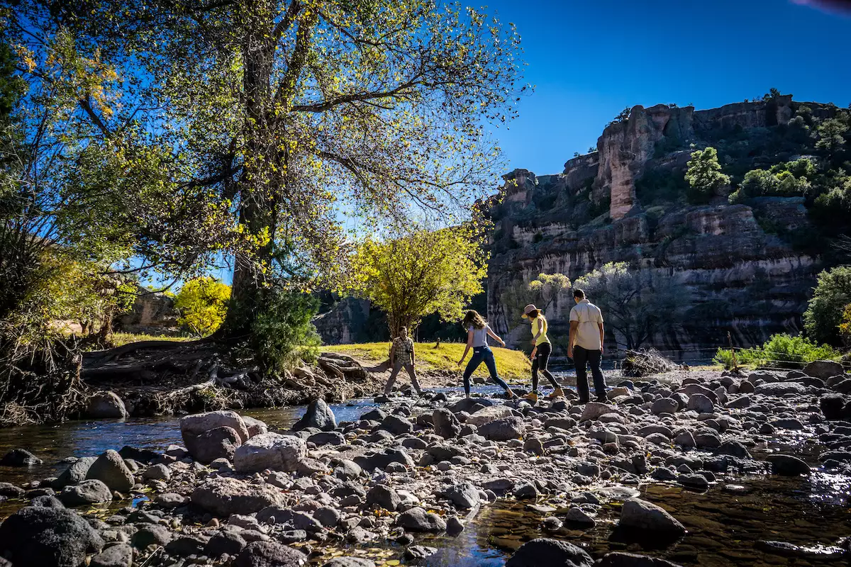 Imagen de cuatro jóvenes cruzando un arroyo y con la sierra de fundo.
