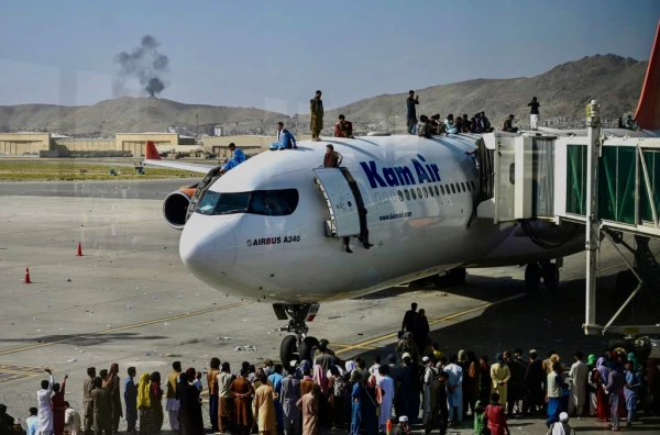 Personas afganas suben arriba de un avión que espera en el avión en el Aeropuerto de Kabul para huir del país tras la toma del poder de los talibanes.