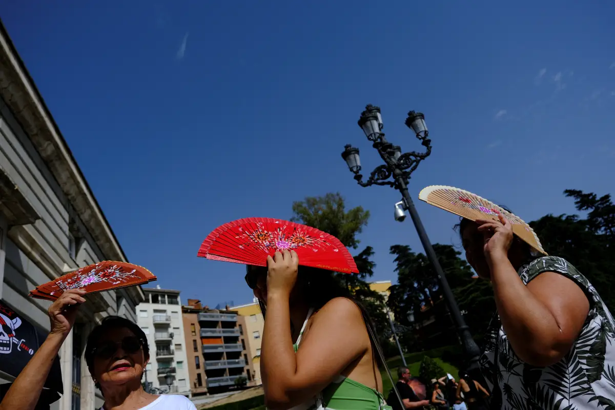 Los ciudadanos peruanos Sadith Ushinagui, de 74 años, Alisson Carrillo, de 29 años, y Carol Ore, de 50, se protegen del sol con los aficionados mientras esperan entrar en el Palacio Real durante la tercera ola de calor del verano en Madrid, España, el 8 de agosto de 2023. REUTERS/Susana Vera