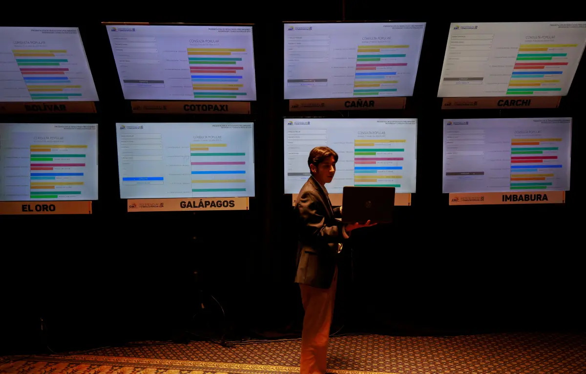 Un periodista mira su computadora portátil frente a una pantalla que muestra los resultados preliminares de un referéndum sobre medidas de seguridad para luchar contra la creciente violencia, en el Centro de Mando del Consejo Nacional Electoral en Quito, Ecuador, el 21 de abril de 2024.