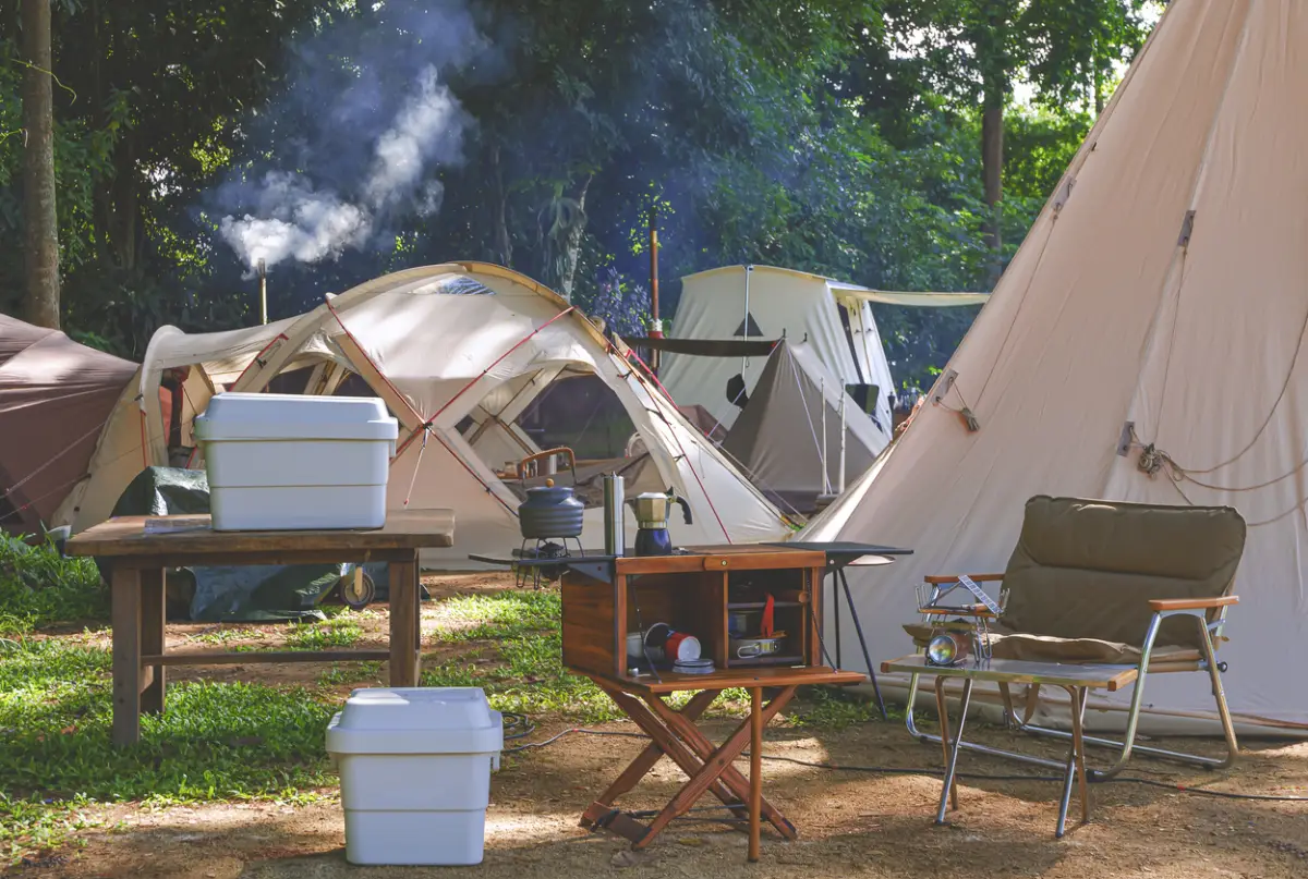 Outdoor kitchen equipment and wooden table set with field tents group in camping area of natural parkland