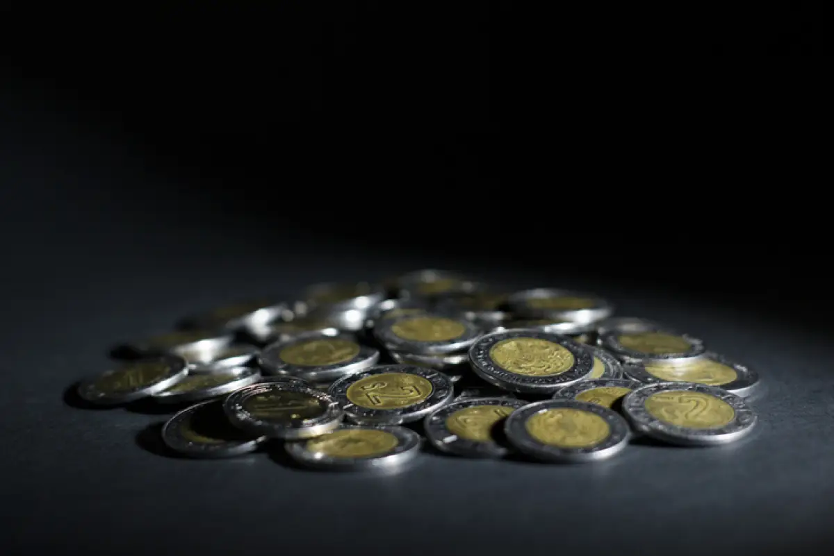 Pila de monedas de un peso con un fondo oscuro.