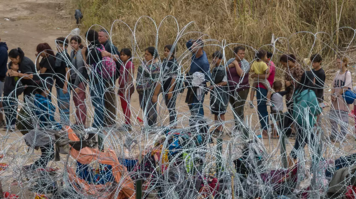 Los migrantes, la mayoría de Venezuela, se paran cerca del alambre de afeitar mientras se entregan a las autoridades después de vadear el río Río Grande hacia los Estados Unidos desde México, en Eagle Pass, Texas, EE. UU., el 5 de octubre de 2023.