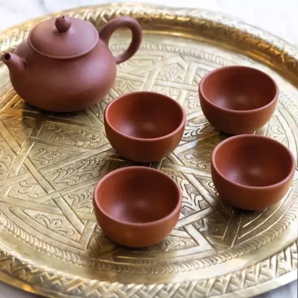 Foto de una charola dorada y redonda con cuatro tazas sin oreja y una tetera.