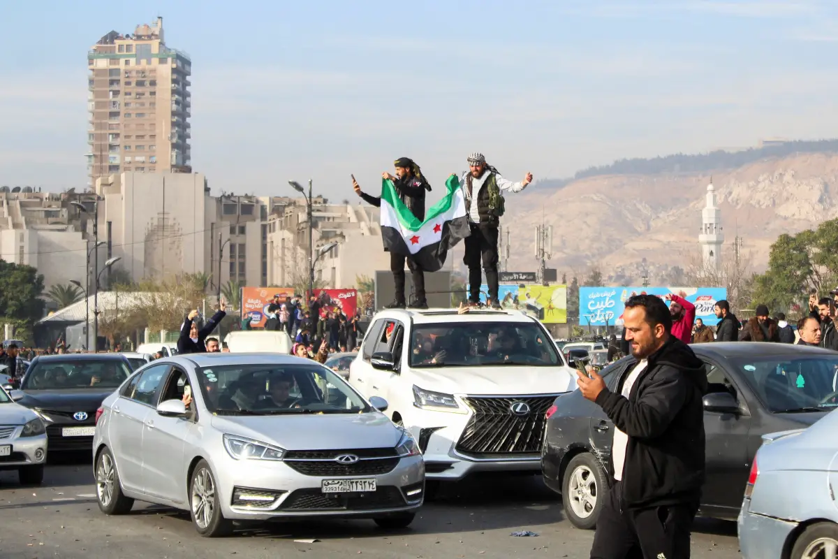 Los hombres sostienen una bandera de la oposición siria en la parte superior de un vehículo mientras la gente celebra después de que los rebeldes sirios anunciaran que habían derrocado al presidente Bashar al-Assad, en Damasco, Siria, el 8 de diciembre de 2024.