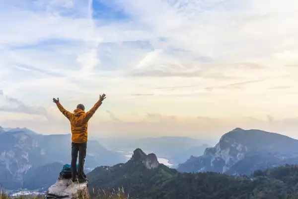 Happy hiker with raised arms on top of the mountain