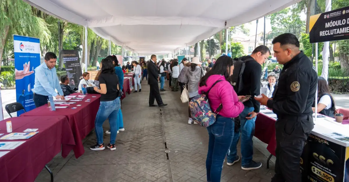 Un pasillo largo al aire libre con mesas al lado y mujeres y hombres hablando, traen folletos en la mano .jpg