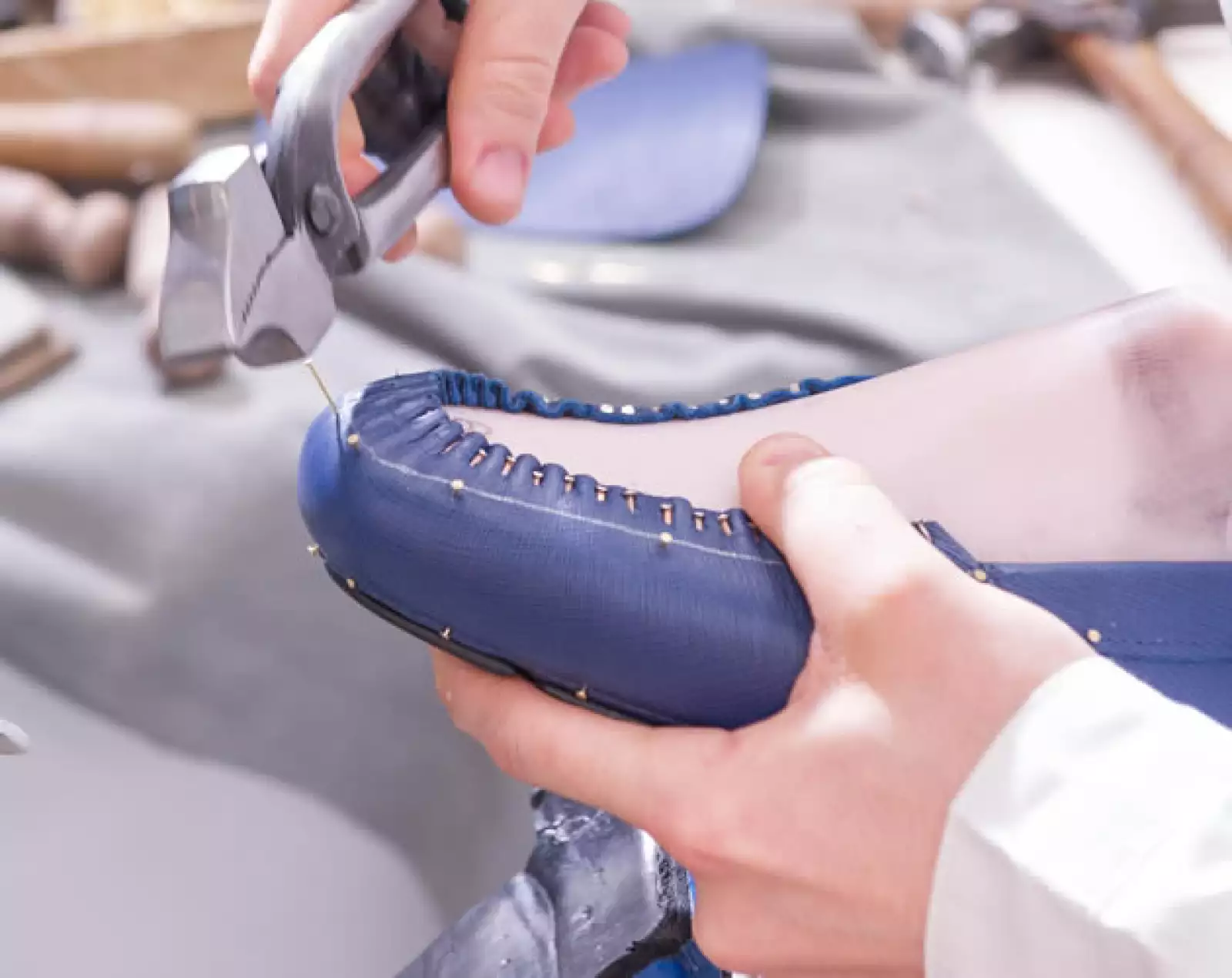 Luego de posicionar la parte superior del zapato sobre la suela de goma, la monta con pegamento. Enseguida, asegura la silueta del zapato clavando delicadas y pequeñas tachuelas.
