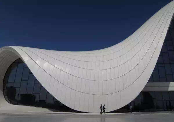 Two people walk across the plaza at the Zaha Hadid designed Heydar Aliyev Center in Baku, Azerbaijan