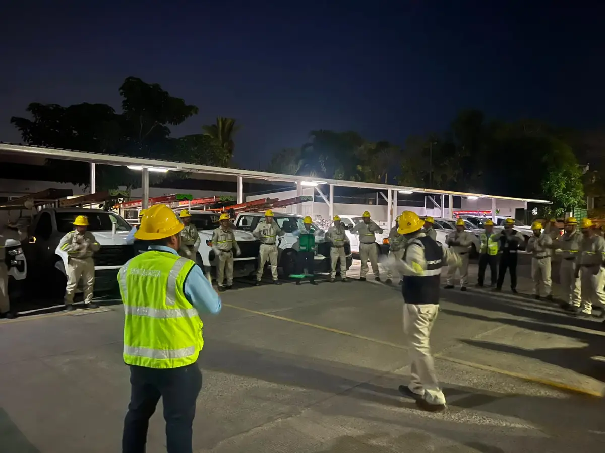 Hombres con uniforme caqui, chalecos y cascos amarillos parados en un patio. El cielo está negro.jpeg