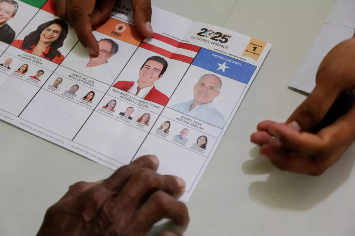 Un trabajador electoral muestra materiales electorales a un votante, una semana tarde en una elección especial después de que el partido gobernante local siguiera votando cerrado el día de las elecciones, en medio de acusaciones de sabotaje y fraude, en una carrera presidencial aún demasiado cerca para llamar mientras continúa el conteo, en San Antonio de Flores, Honduras, el 7 de diciembre de 2025.