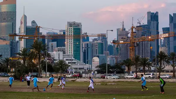 (Trabajadores juegan al fútbol en un área de tierra baldía debajo de los rascacielos de Doha)