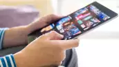 Selective focus at men hand and digital tablet. Young Adult Asian man holding tablet device while choose online movie streaming application with mobile wireless network at home. Entertainment concept.