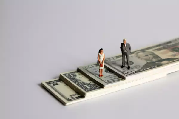 A miniature man and a miniature woman standing on a pile of bills.