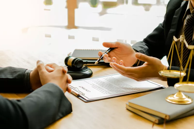 Lawyers discuss business contract documents sitting at a desk in the office of conceptual legal advice. Counselor with hammers and scales of justice on the table.