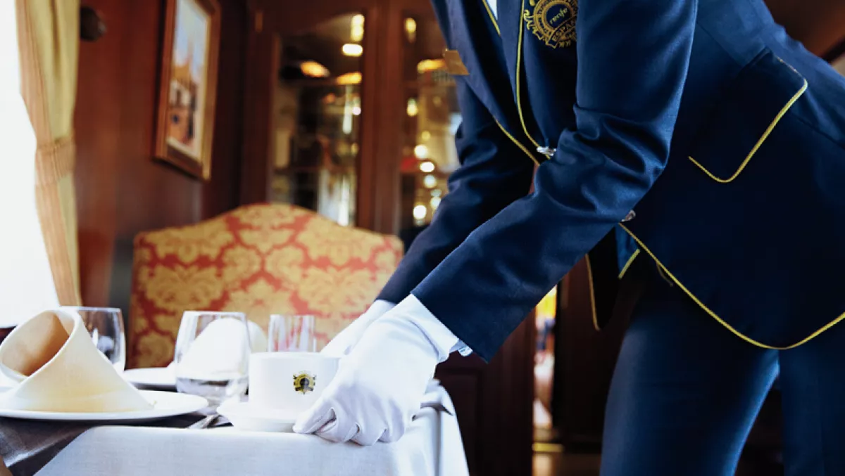 Foto de un mayordomo con guantes blancos recogiendo tazas y vasos de una mesa en un tren de lujo de europa