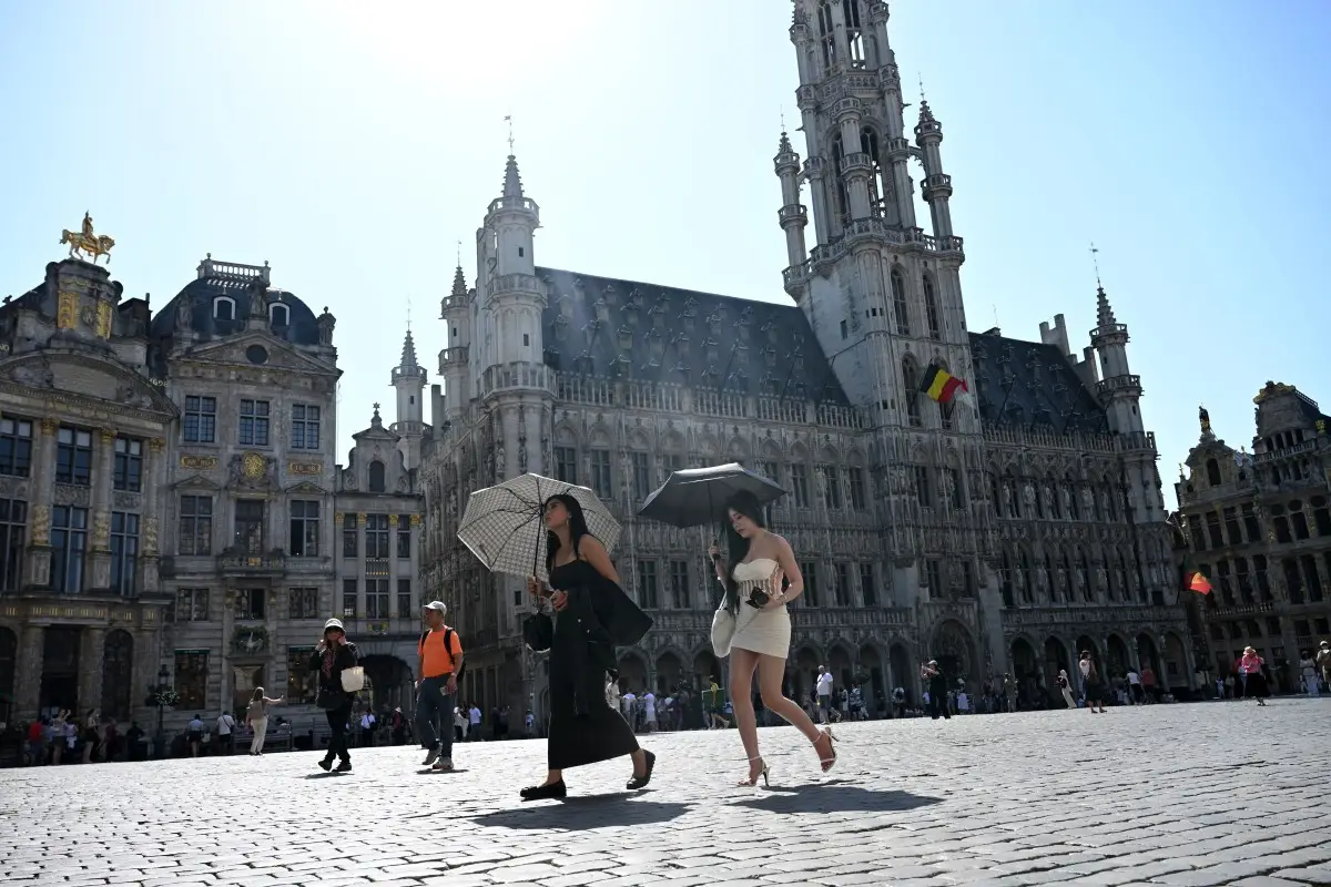 Los turistas caminan bajo sus paraguas para protegerse del sol mientras visitan la Gran Plaza, durante una ola de calor, en Bruselas el 24 de junio de 2026