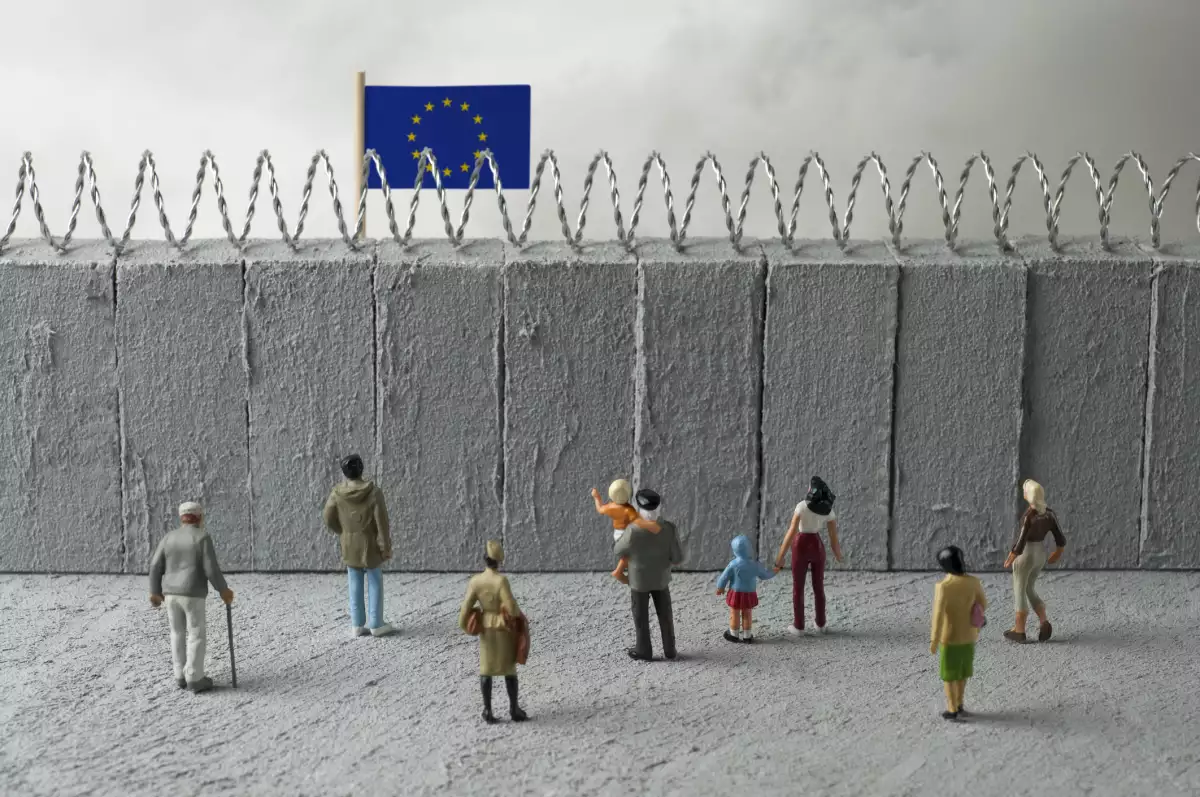 Concepto de crisis de refugiados de la Unión Europea. Personas delante de un muro fronterizo con una bandera de la UE. (Imagen principal del artículo web 'Al igual que Estados Unidos, Europa también endurece sus políticas migratorias').