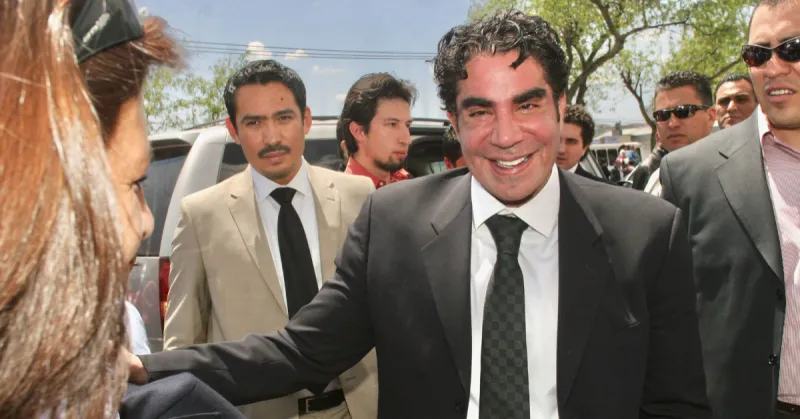Jorge Kahwagi vestido de traje negro y con una sonrisa. Detrás de él otros hombres con traje.jpg