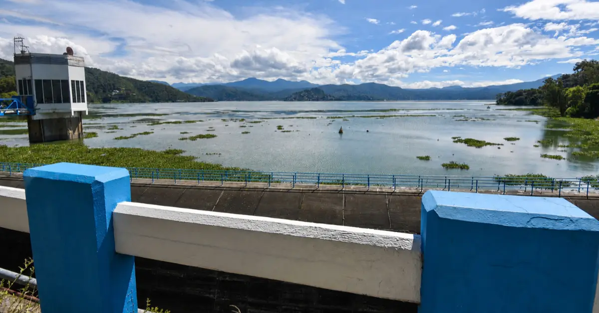 Un cuerpo de agua a cielo abierto; a las orillas hay árboles y una infraestructura en color blanco y azul.jpg