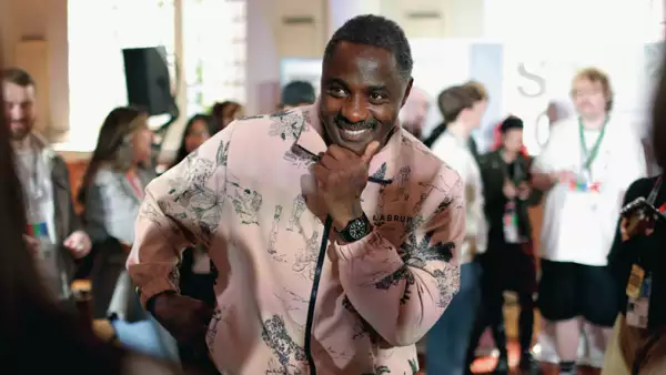 Foto de Idris Elba sonriendo a la cámara con una chaqueta rosada.