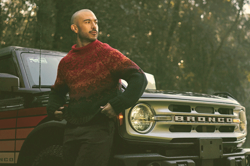 Un hombre con suéter rojo recargado en una camioneta modelo Bronco.gif
