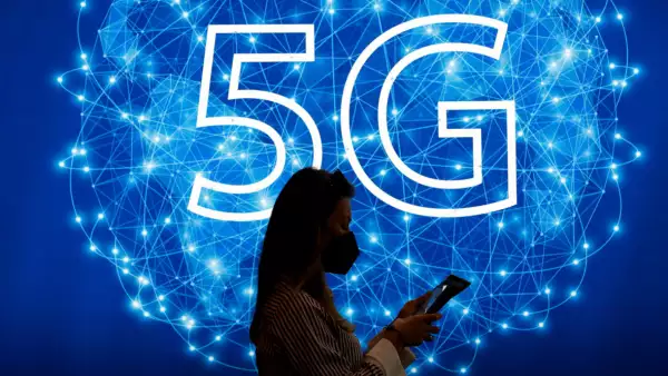 (Una mujer revisa su teléfono frente a un símbolo de 5G)