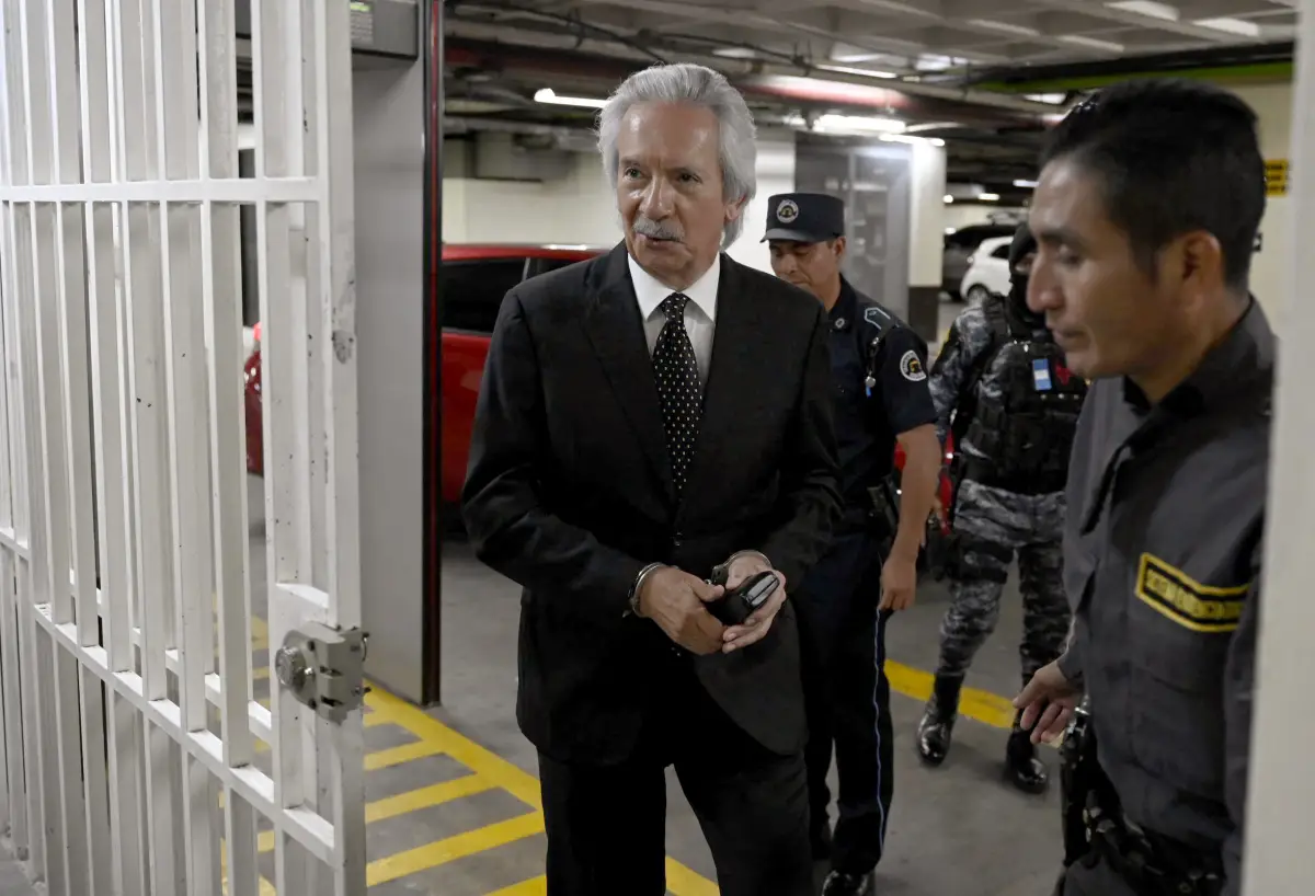 El periodista guatemalteco, José Ruben Zamora de 66 años. Lleva un traje negro, camisa blanca y corbata con puntos, se encuentra esposado. 
Lo escoltan al menos 3 hombres parte de la fuerza militar y policiaca.