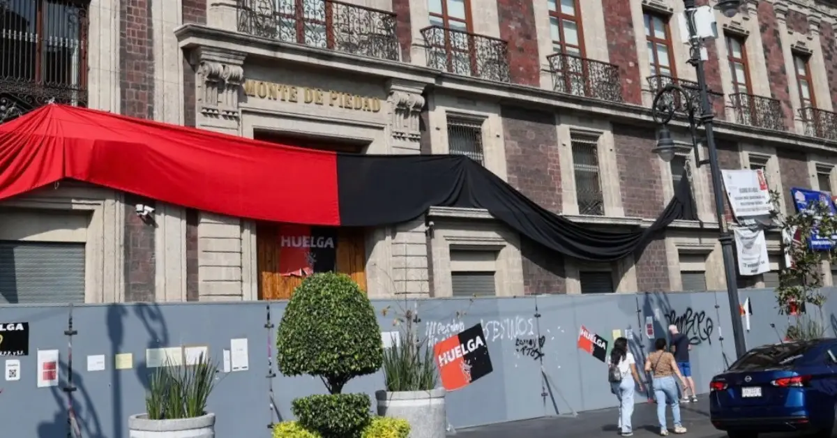 Sucursal cerrada de Nacional Monte de Piedad, con banderas y símbolos rojos y negros, gente camino a las afueras.
