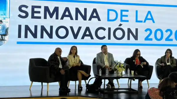 Dos hombres de traje y tres mujeres con vestidos formales frente una mesa de centro. Un letrero con Semana de la Innovación.jpg